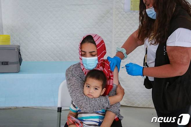 그리스 레스보스 섬의 한 주민이 아이를 안은 채 코로나19 백신 접종을 받고 있다. © AFP=뉴스1