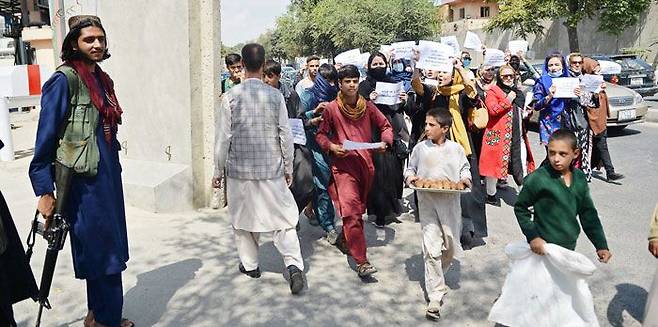 지난 3일(현지 시각) 아프가니스탄 카불에서 부르카를 입지 않거나 얼굴을 드러낸 여성들이 교육과 취업 등 여성 인권 보장을 요구하는 거리 행진을 하면서 총을 든 탈레반 대원(맨 왼쪽) 앞을 지나고 있다. /AFP 연합뉴스