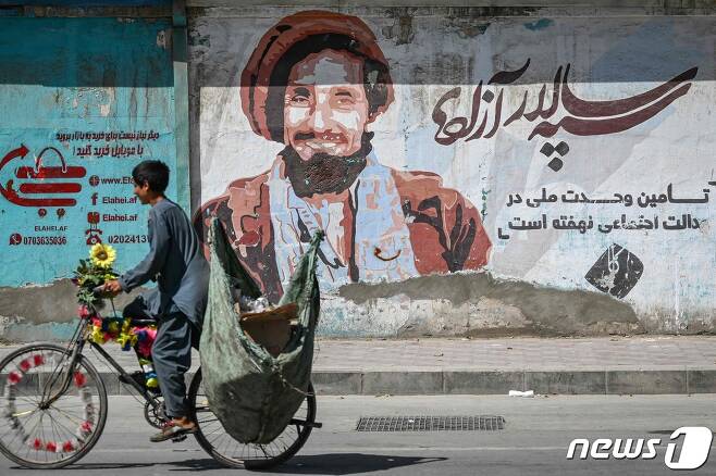 8일 (현지시간) 아프가니스탄 카불에서 '국부' 아흐마드 샤 마수드의 초상화 앞을 청소년이 자전거를 타고 가고 있다. © AFP=뉴스1 © News1 우동명 기자