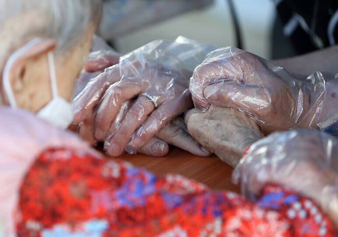 With in-person visits at long-term care facilities being permitted under the special virus countermeasures for the Chuseok holiday, a person in the care of one such facility in Chuncheon, Gangwon Province, holds hands with their daughter and son-in-law during a visit on Wednesday. This is the first time in-person visits at this facility have been permitted in roughly 18 months. (Yonhap News)