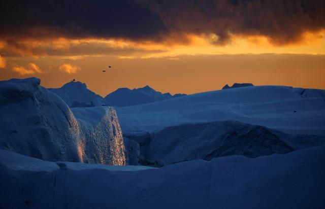 14일 그린란드 디스코만 지역에서 일몰이 진행되는 동안 빙산의 얼음벽에 햇빛이 반사되고 있다. 그린란드=로이터 연합뉴스