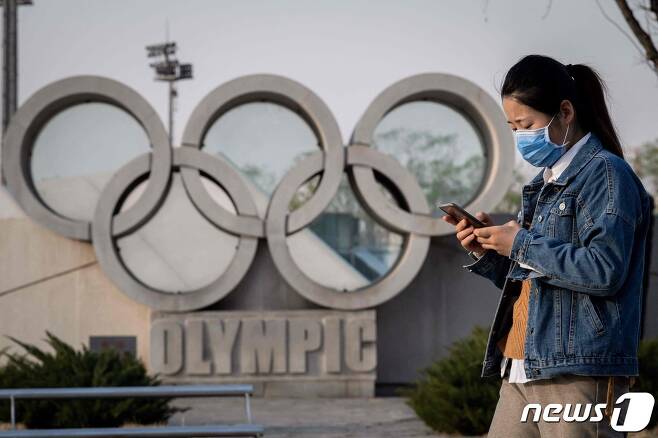 중국 베이징에서 한 여성이 마스크를 쓴 채 올림픽 상징물 앞을 지나고 있다. 2020.03.23 © AFP=뉴스1