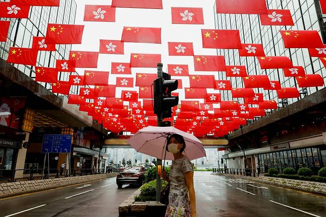 A woman walks under China and Hong Kong‘s flags hanging outside a shopping mall ahead of the 100th founding anniversary of the Communist Party of China, in Hong Kong, China June 28, 2021. REUTERS/Tyrone Siu