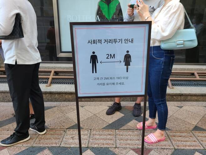 지난 19일 오전 서울 중구 신세계백화점 본점 앞 오픈 런 행렬 중간에 사회적 거리두기를 안내하는 푯말이 세워져 있다.