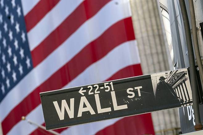 FILE - In this Monday, Sept. 21, 2020, file photo, a Wall Street street sign is framed by a giant American flag hanging on the New York Stock Exchange in New York. Stocks are falling in early trading on Wall Street Monday, Oct. 26, 2020, and deepening last week’s losses. (AP Photo/Mary Altaffer, File)