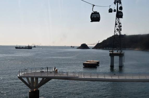 거북섬에서 관광객이 사진을 찍고 있다. 그 위로 케이블카가 운행 중이다.