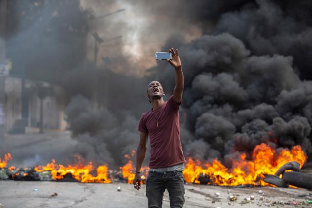 한 아이티 시민이 18일 포르토프랭스의 한 길거리에서 시위대가 낸 불 앞에서 사진을 촬영하고 있다. =포르토프랭스=AP 연합뉴스