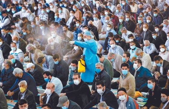 22일(현지시간) 이란의 수도 테헤란의 한 이슬람 사원에서 보건 당국 직원이 마스크를 쓴 채 금요일 기도회에 참석한 사람들 머리 위로 소독제를 뿌리고 있다. 이날 테헤란에서는 코로나19 팬데믹으로 중단됐던 금요일 기도회가 처음으로 다시 열렸다. [AFP=연합뉴스]