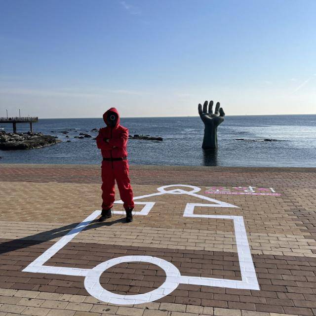 경북 포항시가 지난달 28일 해돋이 명소인 호미곶을 알리기 위해 해맞이 광장에 인기 드라마 오징어 게임의 상징 문양을 바닥에 그려 넣고 오징어 게임 의상을 입은 안내요원을 배치했다. 포항시 제공