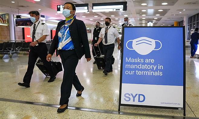 28일(현지시간) 호주 시드니 공항 터미널에 '마스크 착용 의무' 안내판이 설치돼 있는 가운데 여객기 승무원들이 이동하고 있다. 시드니=AP연합뉴스