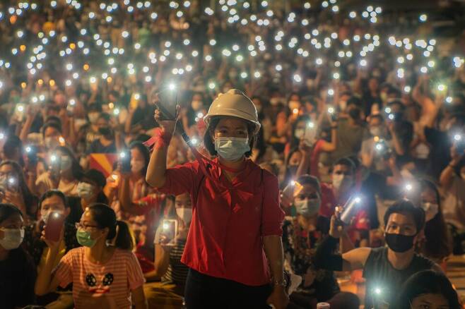 미얀마 시민들이 3월14일 양곤 도심에서 휴대전화 플래시를 켜서 흔들며 저항의 노래를 부르고 있다. 헬멧을 쓴 여성이 손목에 두른 붉은 리본은 비폭력의 상징이다.