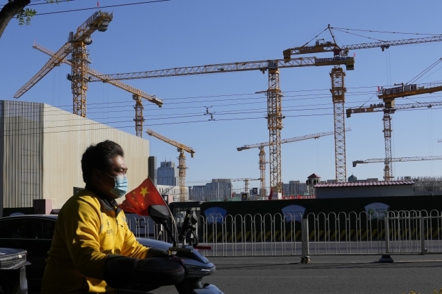 지난 10월 중국 베이징에 있는 한 건설 현장 앞으로 배달원이 중국 국기를 단 오토바이를 타고 지나가고 있다. AP연합뉴스