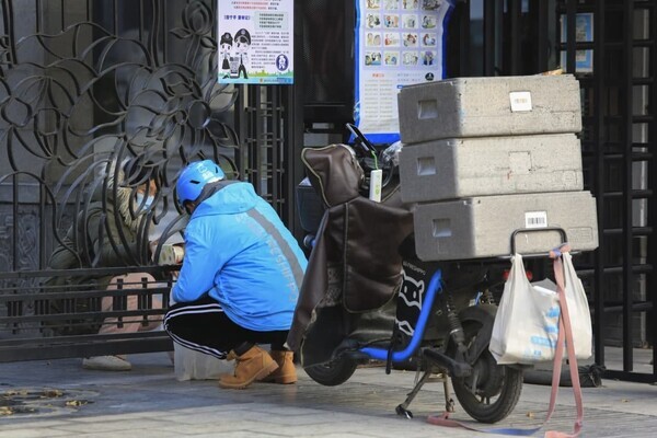 봉쇄식 관리 20일째를 맞은 11일 중국 산시성 시안의 한 주거단지 들머리에서 배달 노동자가 굳게 닫힌 문 사이로 마스크를 쓴 주민에게 물품을 전달하고 있다. 시안/AP 연합뉴스