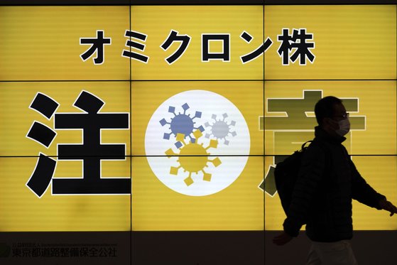 13일 일본 도쿄에서 마스크를 쓴 시민이 오미크론 변이 유행을 경고하는 내용의 전광판 앞을 지나고 있다. [AP=연합뉴스