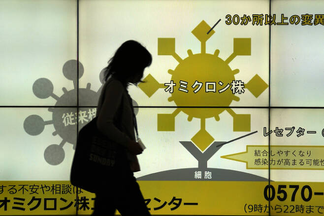 도쿄의 한 여성이 오미크론 변이의 강한 전염력을 경고하는 게시판 앞을 지나고 있다. 도쿄=AP연합뉴스