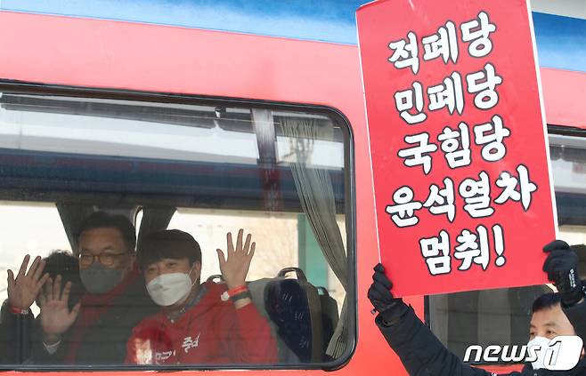 이준석 국민의힘 대표가 11일 오전 열정열차 출발을 위해 충남 천안역에서 정진석 의원과 함께 열차에 올라 손인사 하고 있는 가운데 밖에서 전국철도노조 조합원이 열정열차를 반대하는 피켓을 들고 있다. 2022.2.11/뉴스1 © News1 김기태 기자