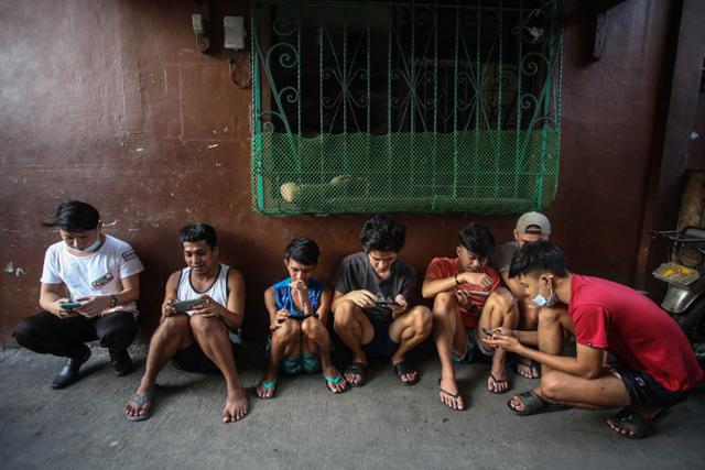 필리핀 사람들이 지난해 12월 마닐라 근교 마을 골목에서 NFT 게임을 하고 있다. 필리핀에서는 코로나19로 생계가 막막해진 이들 중 게임 아이템을 팔아 돈을 벌 수 있는 액시 인피니티 게임으로 생계를 잇는 이들도 적잖다. 마닐라=AFP 연합뉴스