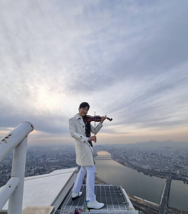 뮤지컬 '지붕 위의 바이올린'에 출연하는 배우 콘이 롯데월드타워 옥상에서 바이올린을 연주하고 있다. "공중에 붕 떠 있는 느낌이었어요. 바람도 불고 날씨가 추워 코트 안에 핫팩을 잔뜩 넣고 촬영했습니다." /HJ컬쳐