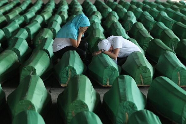 보스니아 스레브레니차 학살 10주기를 맞아, 그동안 신원이 확인된 시신 600여 구를 정식 매장하는 집단장례식이 열렸다. 녹색의 물체는 모두 관이다. 두 무슬림 여인이 엎드려 울고 있다. 2005년 7월. (사진: 게티이미지 코리아)