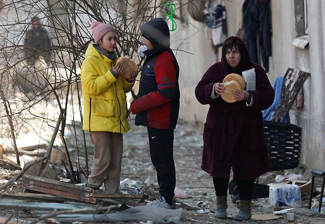 우크라이나 남부 항구도시 마리우폴 주민들이 28일(현지 시각) 파괴된 건물 밖에 서서 빵을 먹고 있다. /로이터 연합뉴스