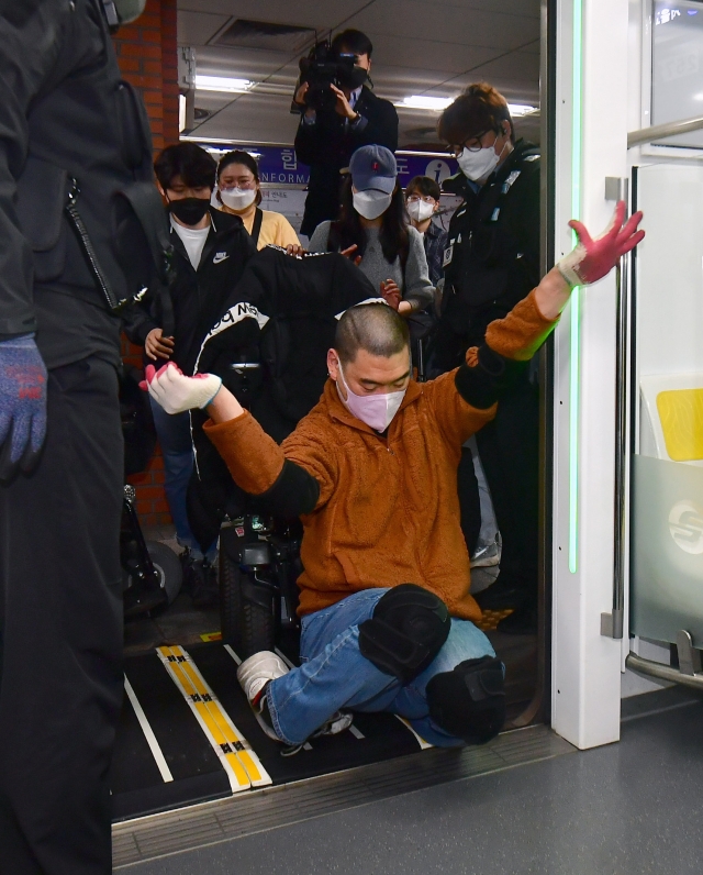 한 전장연 회원이 휠체어에서 내려 무릎으로 어 열차에 들어가고 있다.