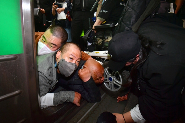 출근길 지하철 탑승 시위를 벌인 전장연 회원들이 휠체어에서 내려 지하철 열차 문을 기어서 통과하면서 뒤엉켜 있다.