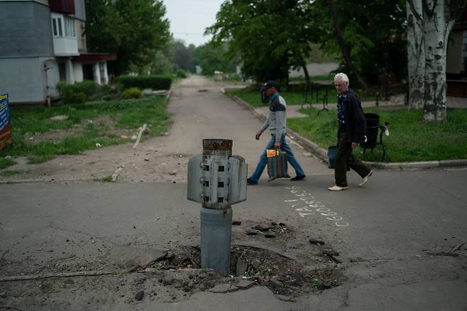 13일(현지시각) 우크라이나 루한스크주 리시찬스크에서 주민들이 도로에 박힌 로켓 주변을 지나고 있다./AP