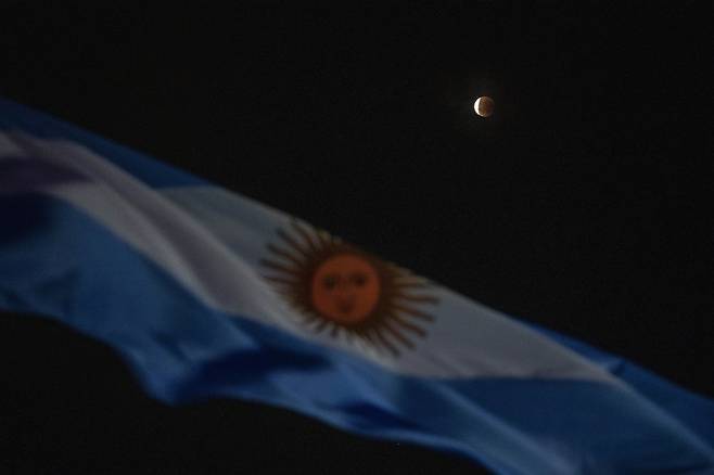 지난 16일 아르헨티나 부에노스아이레스에서 국기 뒤로 관측된 달의 모습. 사진=AP 연합뉴스