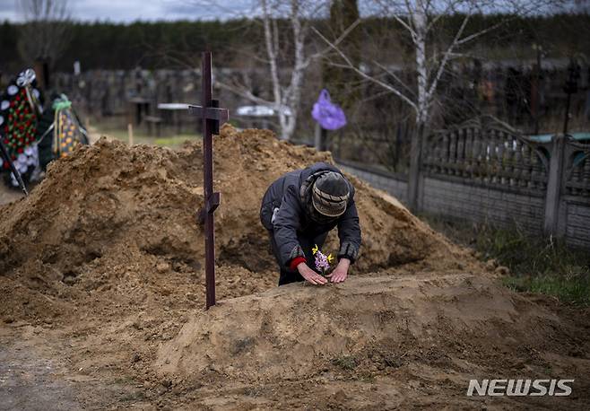 [부차=AP/뉴시스] 지난달 19일(현지시간) 우크라이나 부차에서 한 여인이 남편의 무덤에 꽂을 꽂고 있다. 2022.05.24.