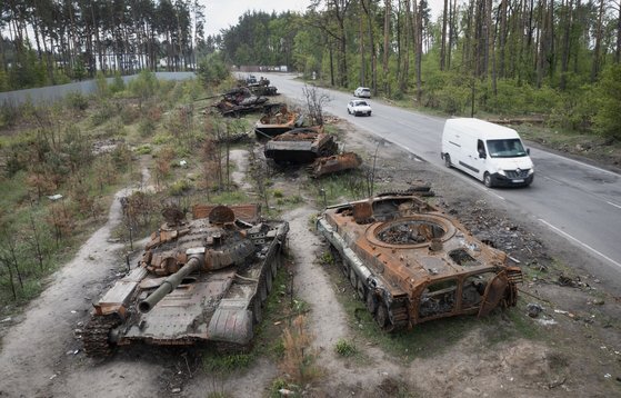 지난 23일 우크라이나 수도 키이우 인근 도로에서 파괴된 탱크들 옆으로 자동차가 지나가고 있다. AP=연합뉴스