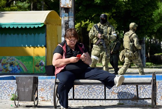 러시아군이 장악한 우크라이나 남부 헤르손주의 한 주민이 지난 20일 경계에 나선 러시아군 앞에 앉아있다. [AFP=연합뉴스]