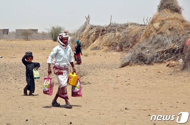 수 백만명이 기아 위기에 처해있는 홍해 연안 예멘 호데이다 서부 헤이스 지역 난민 캠프에서 구호 식량과 물품을 들고 한 남성과 아이가 걸어가고 있다. 2022.03.29 © AFP=뉴스1 © News1 정윤미 기자