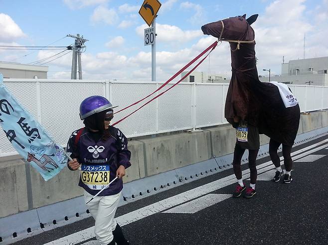 2014년 일본 고베마라톤에서 말과 기수로 분장한 아마추어 마라토너들이 달리고 있다. 이들이 말에게 붙인 이름은 ‘칩 임팩트(Cheap Impact)’로 전설적인 경주마 ‘딥 임팩트(Deep Impact)’의 패러디다.ⓒ이범준 제공