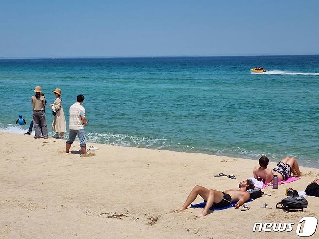 강원 강릉 경포해변에서 햇볕을 쬐고 있는 외국인 관광객 뒤로 바다에 모터보트가 지나가고 있다(뉴스1 DB)