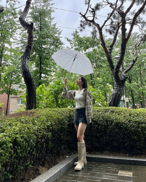 Bona in the open photo is staring at the camera while wearing an umbrella outdoors.