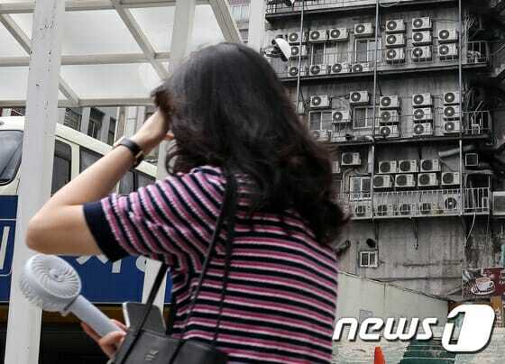 전국에 때이른 폭염이 지속되는 4일 서울 시내 한 건물 외벽에 가득 매달린 에어컨 실외기 앞으로 한 시민이 휴대용선풍기로 더위를 식히며 지나가고 있다.