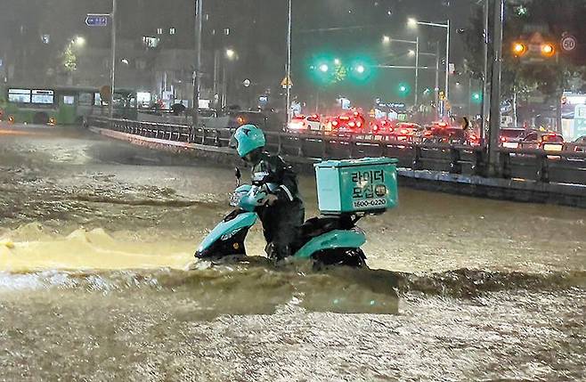 8일 서울 관악구 도림천이 범람해 이날 오후 9시쯤 관악구에서는 주민들에게 ‘대피령’이 내려지기도 했다. 한 배달원이 빗물이 넘실대는 도림천 인근에서 반쯤 잠긴 오토바이를 몰고 있다. /뉴스1