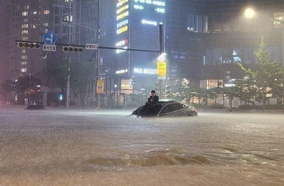 폭우가 쏟아진 8일 서울 서초동 아파트 단지 앞에서 한 남성이 침수된 차량 위로 올라가 몸을 피하고 있다. 온라인커뮤니티 캡처