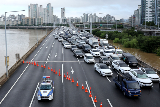 As the Han River rises because of torrential rain overnight, a police patrol car blocks several lanes near the river on the Olympic Highway near Mapo Bridge in Seoul Wednesday morning. [YONHAP]