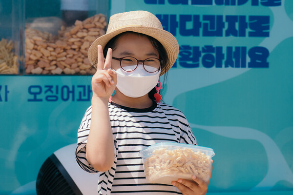 해안쓰레기를 과자로 바꿔주는 환경재단 ‘씨낵 캠페인’에 참여한 어린이가 씨낵 트럭 앞에서 과자를 담은 다회용기를 들고 있다. 환경재단 제공