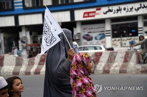 아프간 칸다하르에서 한 여성이 부르카를 착용한 채 탈레반 상징 깃발을 든 모습 [AFP 연합뉴스 자료사진. 재판매 및 DB 금지]