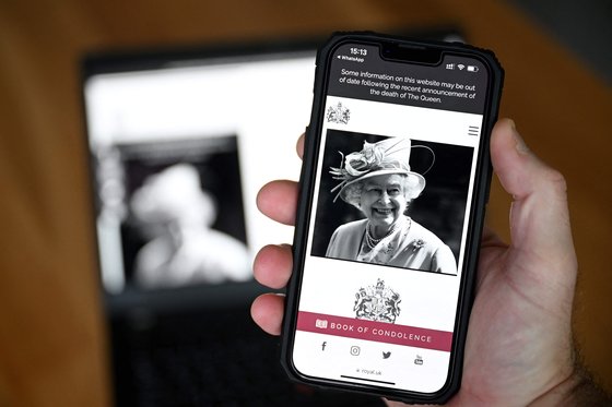 한 시민이 엘리자베스 2세 여왕의 서거를 알리는 영국 왕실 공식 조문록 홈페이지를 휴대전화로 보고 있다. [AFP=연합뉴스]