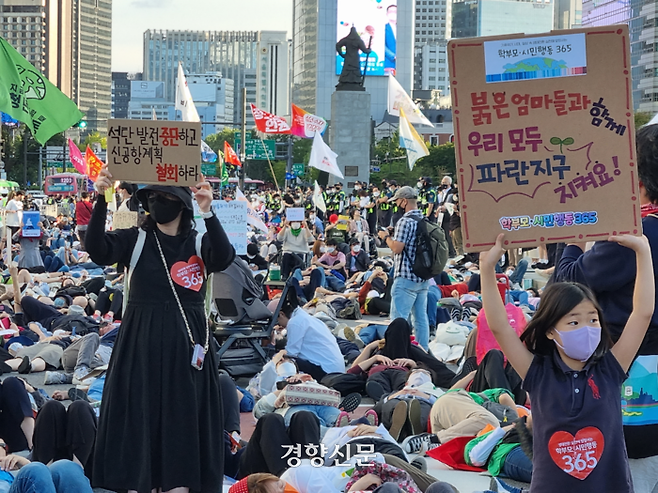 24일 기후정의행진에 참여한 시민들이 서울시청 인근에서 죽은 듯이 눕는다는 뜻의 ‘다이-인(Die-in)) 시위를 하는 도중 두 시민이 서서 종이상자로 만든 손팻말을 들고 있다. 강한들 기자