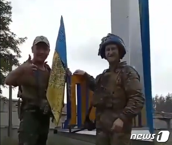 우크라이나 군인 2명이 도네츠크주 리만의 도시 표지판에 국기를 꽂고 있다. 우크라이나 대통령 비서실 제공 동영상 캡처.