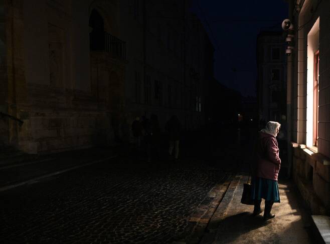 2022년 11월 23일(현지시간), 폴란드 국경에 접하고 있는 우크라이나 서부 도시 르비우에서 한 여성이 전기가 끊긴 거리를 걷고 있다. 우크라이나 당국은 러시아군이 11월 23일 전국의 목표물에 70여발의 크루즈 미사일을 발사하고 공격 드론을 띄웠다고 밝혔다. /AFP 연합뉴스