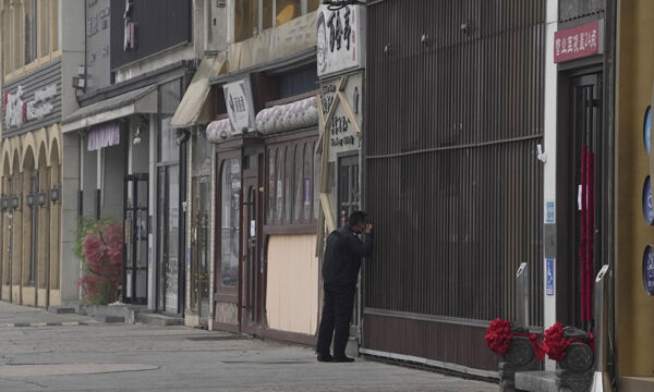 24일 중국 베이징에서 한 경비원이 문 닫은 상점의 셔터 사이를 들여다보고 있다. 베이징=AP뉴시스