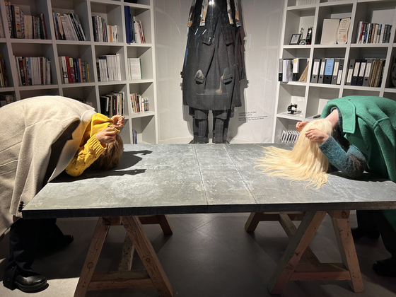 Two lifelike mannequins that are bowing to each other on opposite sides of a table. The one wearing an ivory coat embodies Solid Homme and the other wearing a green coat represents Wooyoungmi. [SHIN MIN-HEE]