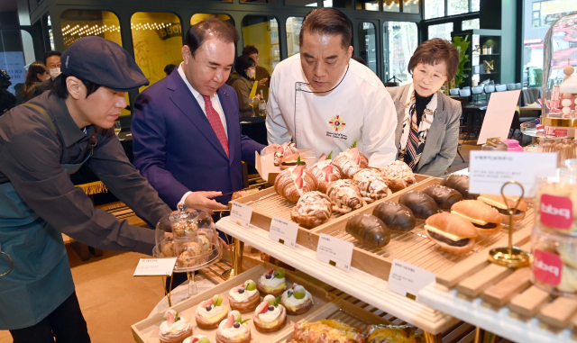 윤홍근(왼쪽 두번째) 제너시스BBQ 회장이 6일 서울 송파구 'BBQ 빌리지' 송리단길점에서 열린 오픈행사에 참석해 관계자의 설명을 들으며 빵을 고르고 있다. 이호재 기자