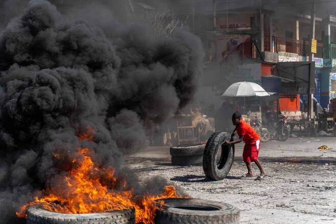 범죄단체에 대한 대책을 촉구하며 경찰관들이 폭동을 일으킨 아이티의 수도 포르토프랭스의 한 도로에서 시위 참가자가 타이어를 나르고 있다. [AFP 연합]