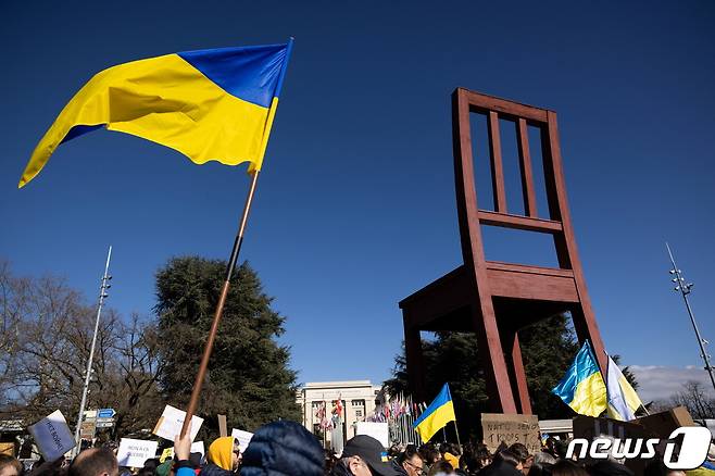 우크라이나를 지지하는 시위대가 26일(현지시간) 스위스 제네바 유엔사무소 앞에서 시위하고 있다. 시위대가 전쟁에서 희생된 민간인을 상징하는 '부러진 의자' 앞에서 우크라이나 국기를 흔들고 있다. 2022.02.26/news1 ⓒ 로이터=뉴스1 ⓒ News1 김민수 기자